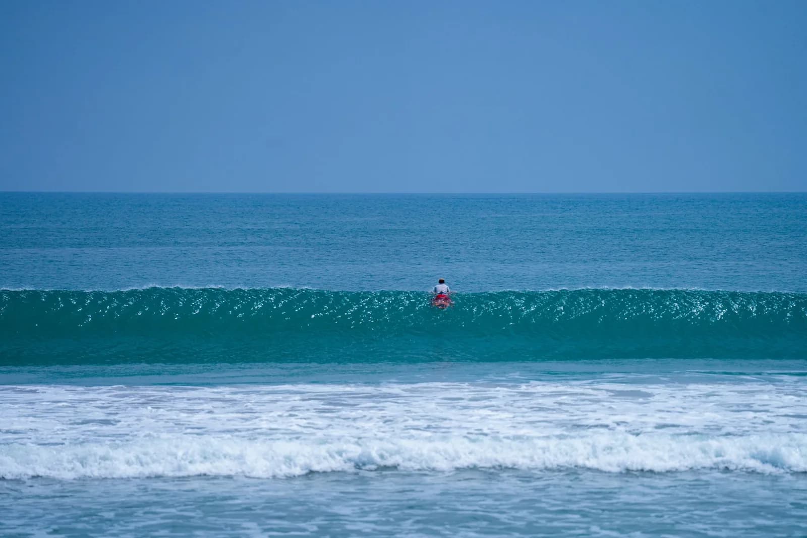 Vague qui déferle sur la côte ouest de Bali avec un surfeur qui passe la barre, houle constante devant les plages de Seminyak et Kuta