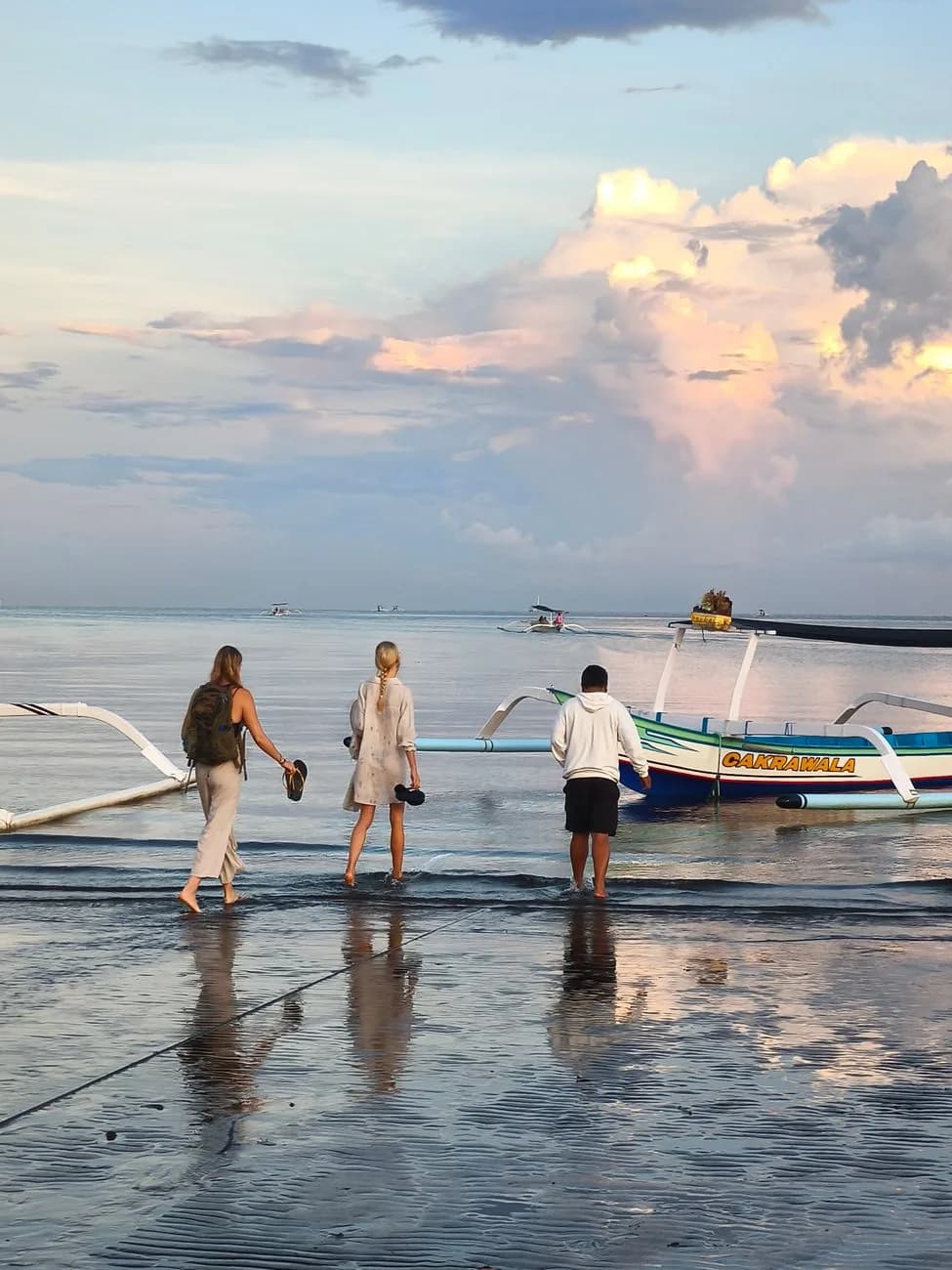Voyageurs chaussures à la main s'apprêtant à embarquer sur un bateau traditionnel au lever du jour sur une plage de Bali
