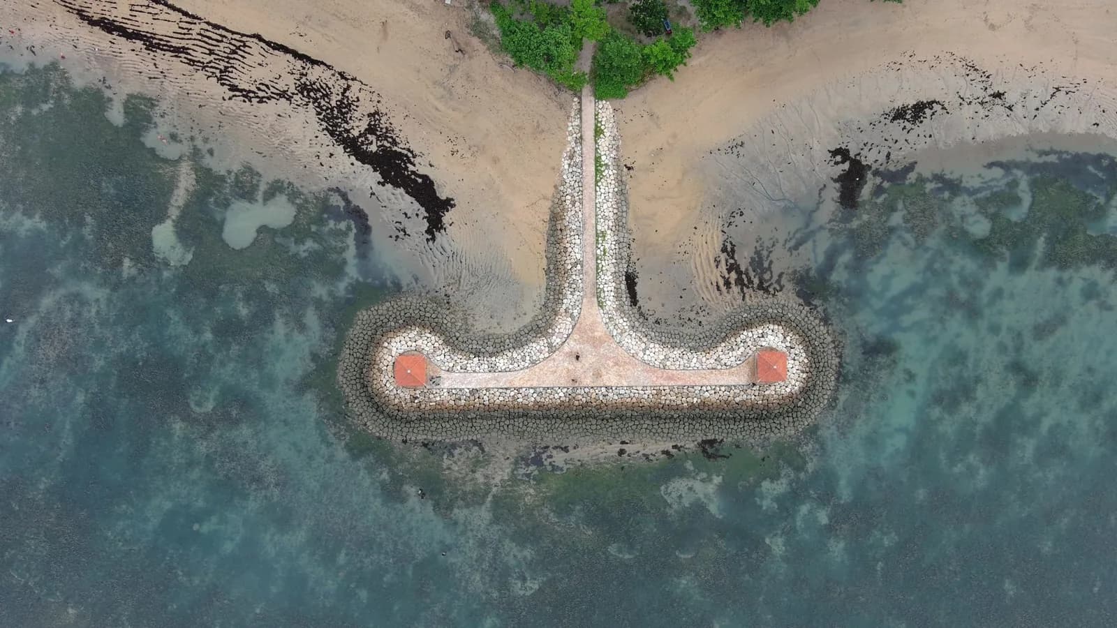 Vue aérienne d'une jetée de pierre en T à Sanur à marée basse, avec le platier de corail et les bancs d'algues découverts autour