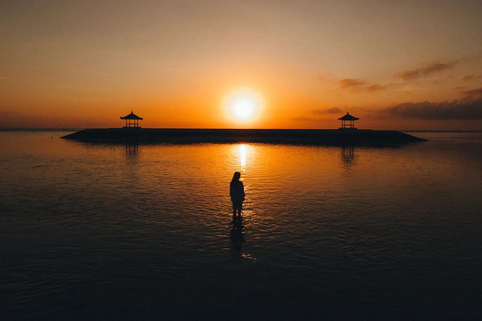 Lever de soleil sur la mer à Sanur, silhouette des deux bale de la jetée et d'une baigneuse dans le lagon