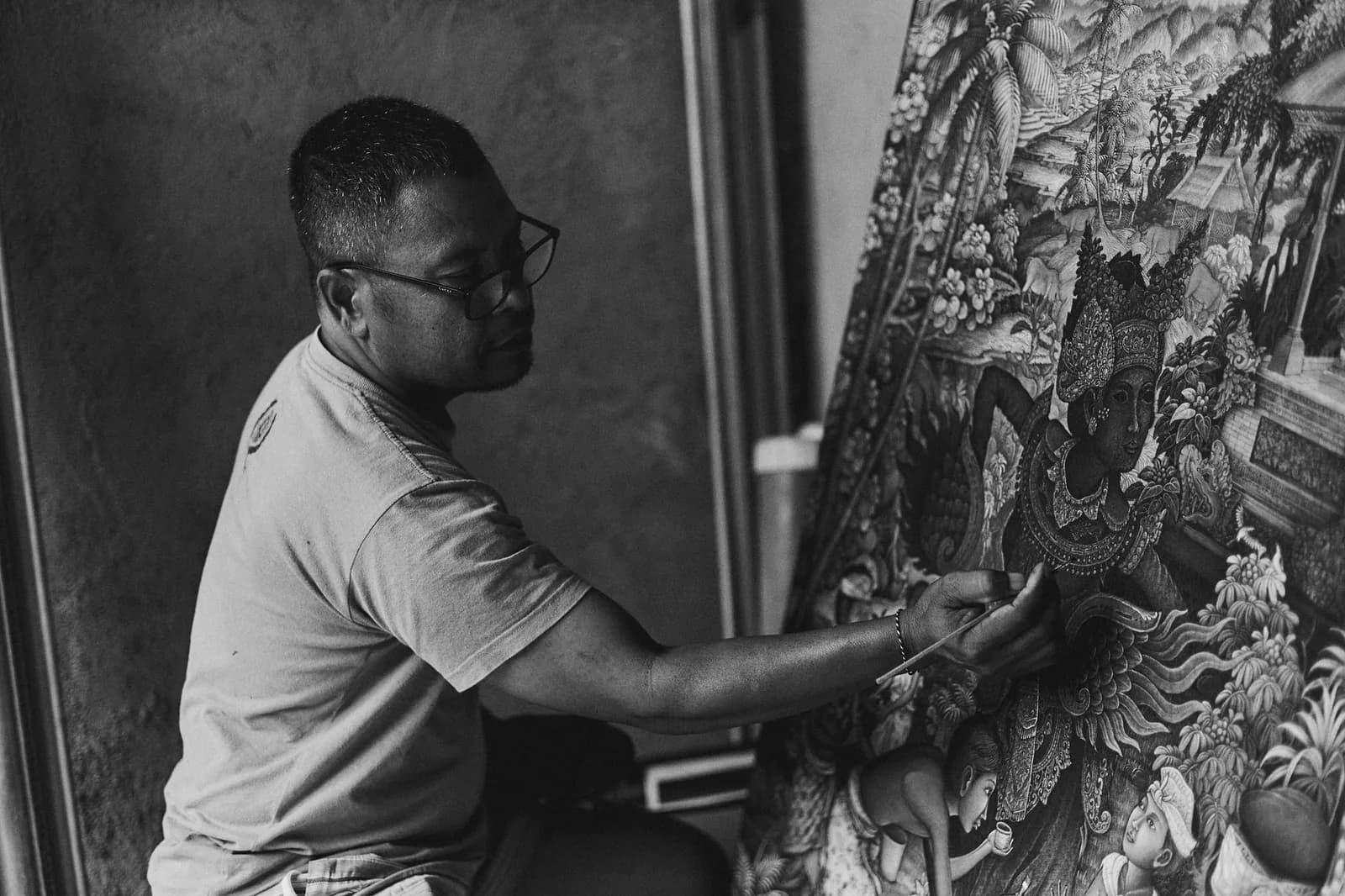 Peintre balinais travaillant au pinceau une toile traditionnelle très détaillée, comme celles exposées au musée Le Mayeur de Sanur