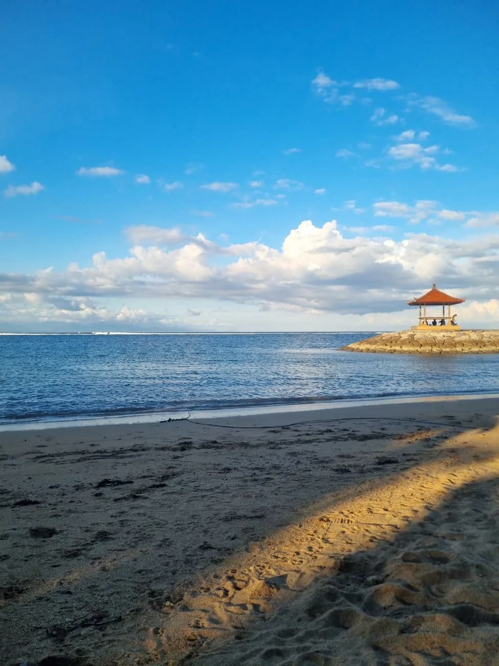 Plage de Sanur à Bali en plein jour, bale sur la jetée de pierre et ligne blanche du récif barrière visible au large