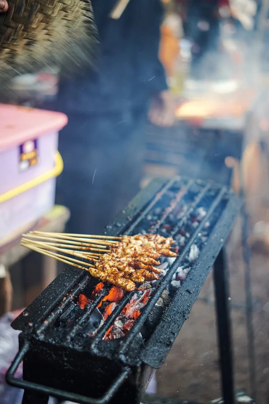 Brochettes de sate grillées sur un long brasero à charbon dans un marché de nuit indonésien, comme au Sindhu Night Market de Sanur