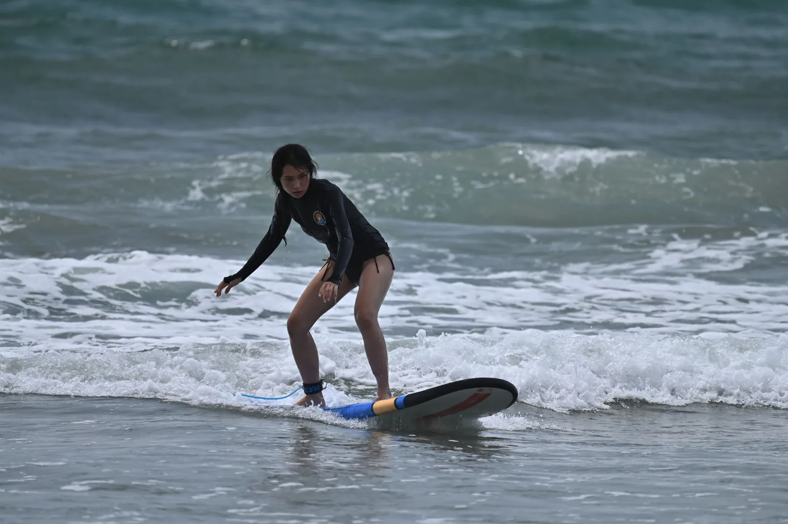 Débutante en cours de surf sur la mousse d'une vague, sur la côte ouest de Bali près de Seminyak