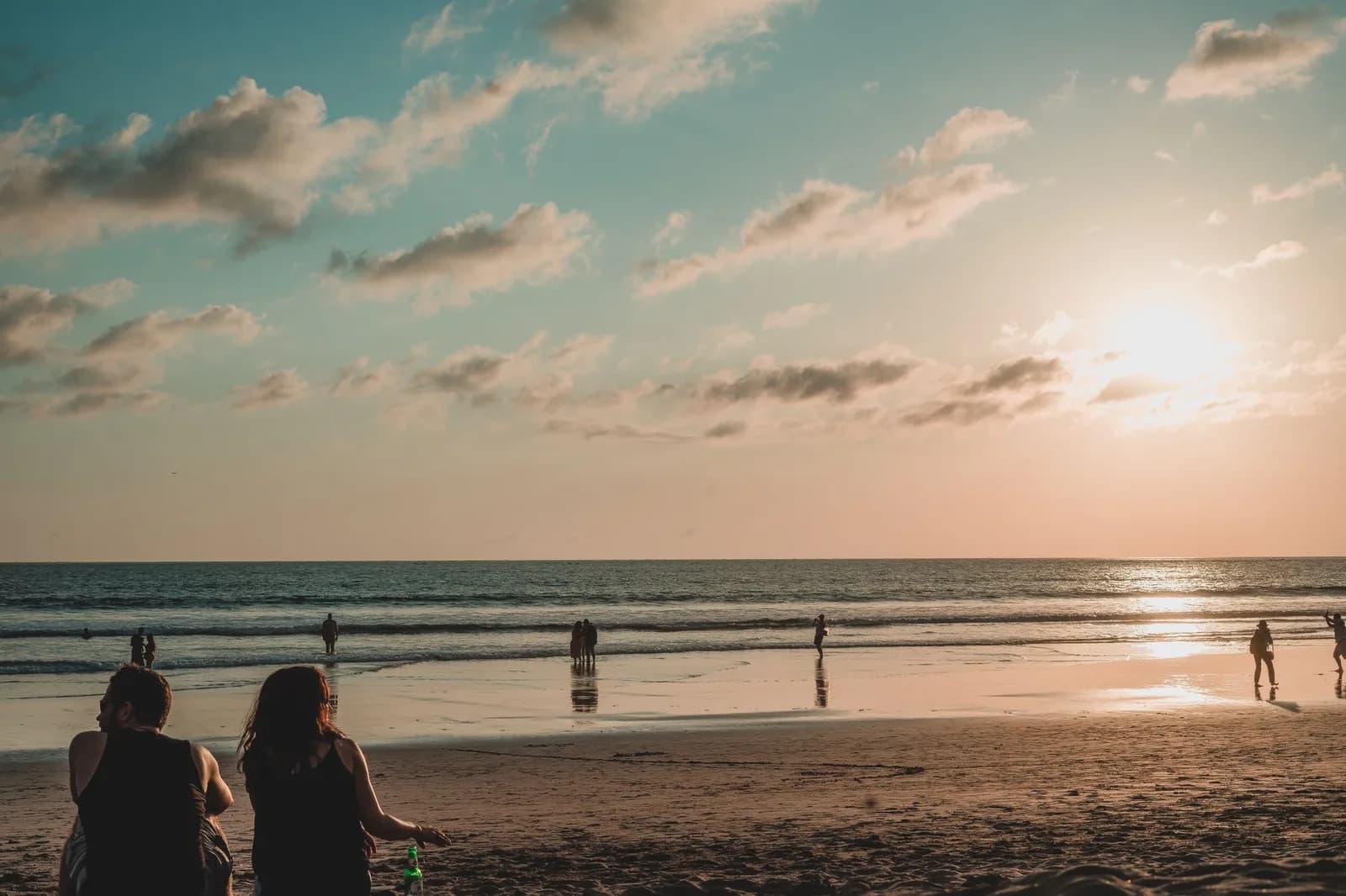 Plage de sable large de la côte ouest de Bali en fin de journée à Seminyak, promeneurs sur le sable mouillé et rouleaux au large