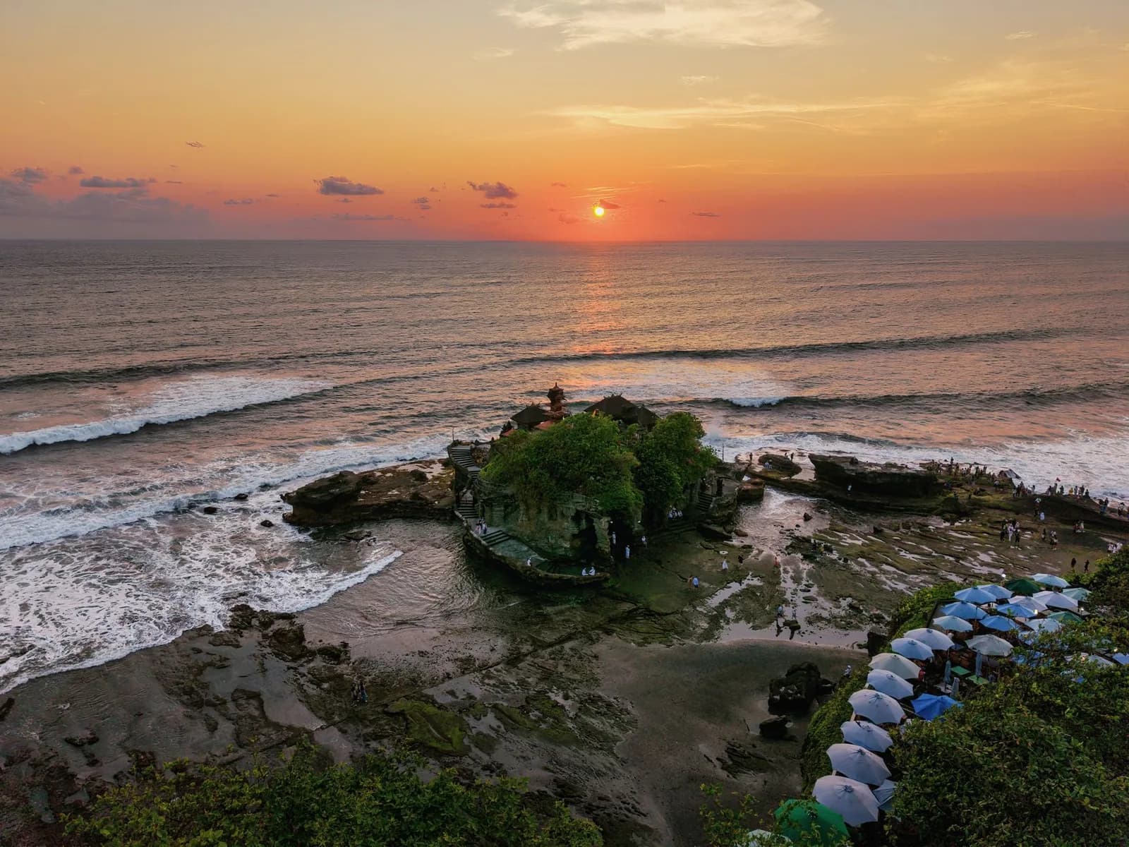 Vue aérienne du temple de Tanah Lot au coucher du soleil avec les visiteurs sur le platier, Bali
