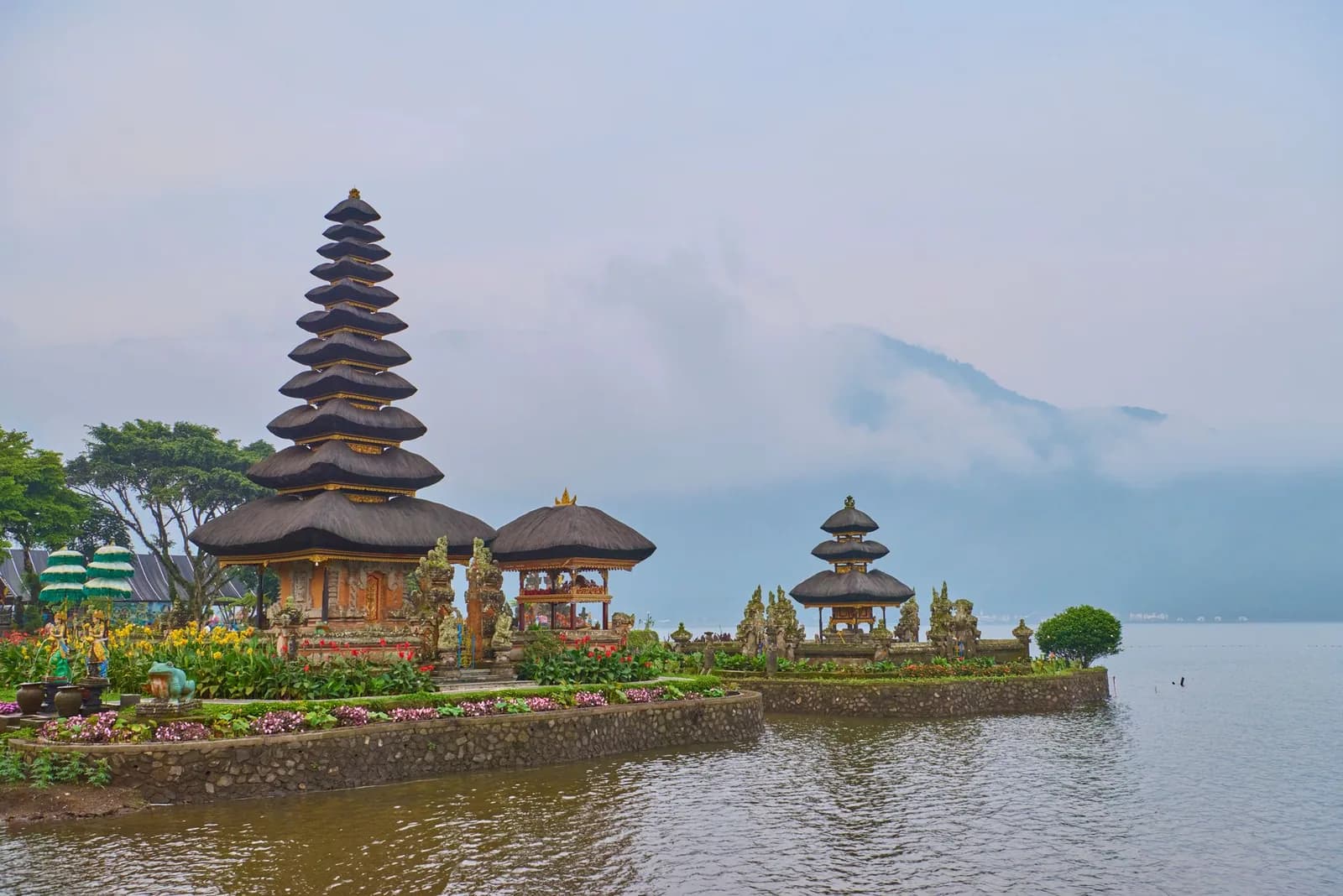 Les pagodes d'Ulun Danu Beratan au petit matin, brume sur les montagnes et jardins fleuris au bord du lac Bratan, Bali