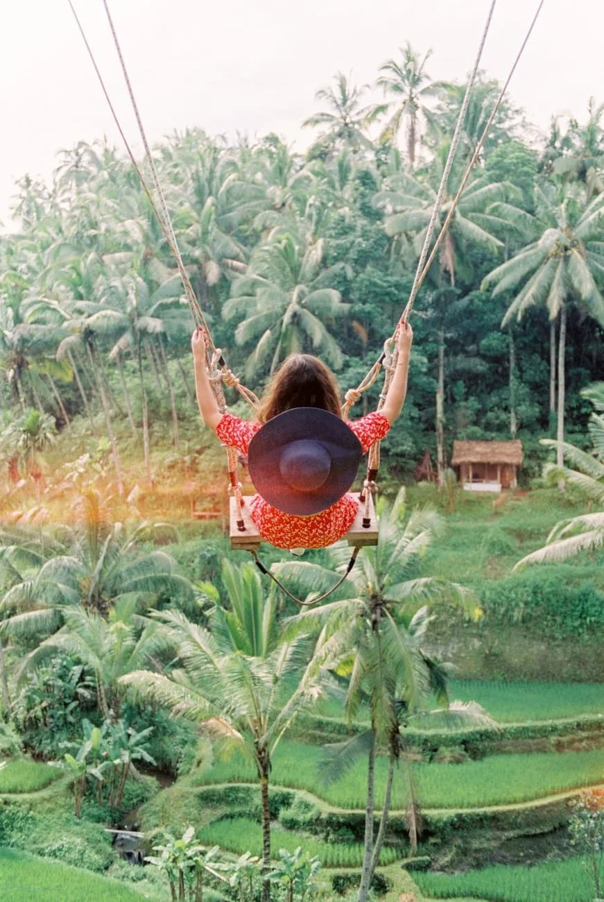 Femme en robe rouge et chapeau sur une balançoire de Bali au-dessus des rizières et des palmiers près d'Ubud