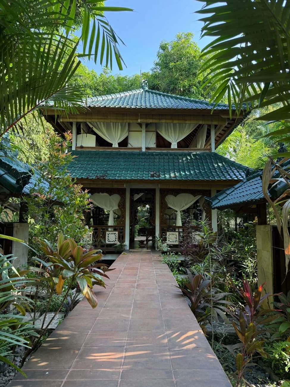 Pavillon ouvert d'une villa balinaise traditionnelle à Bali, toiture en tuiles vernissées et allée bordée de plantes tropicales