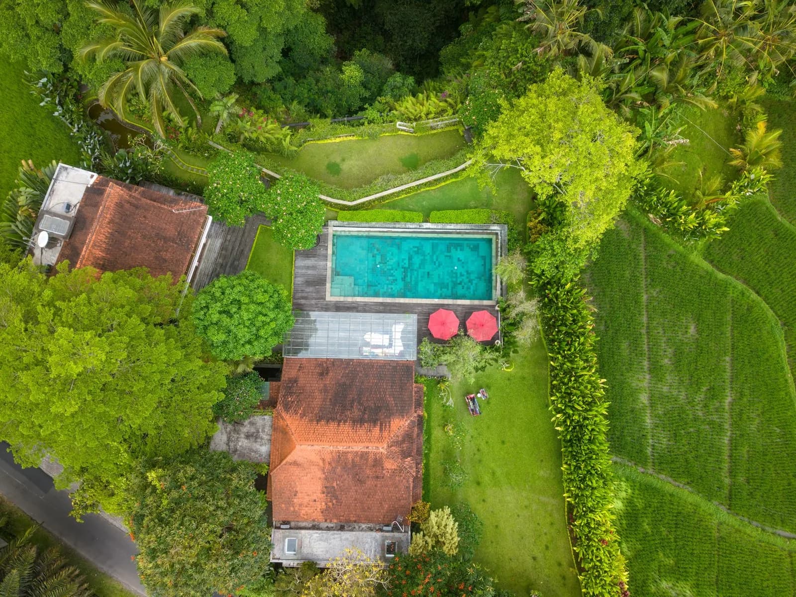 Vue aérienne d'une villa balinaise avec piscine privée, jardin et toitures en tuiles, bordée de rizières