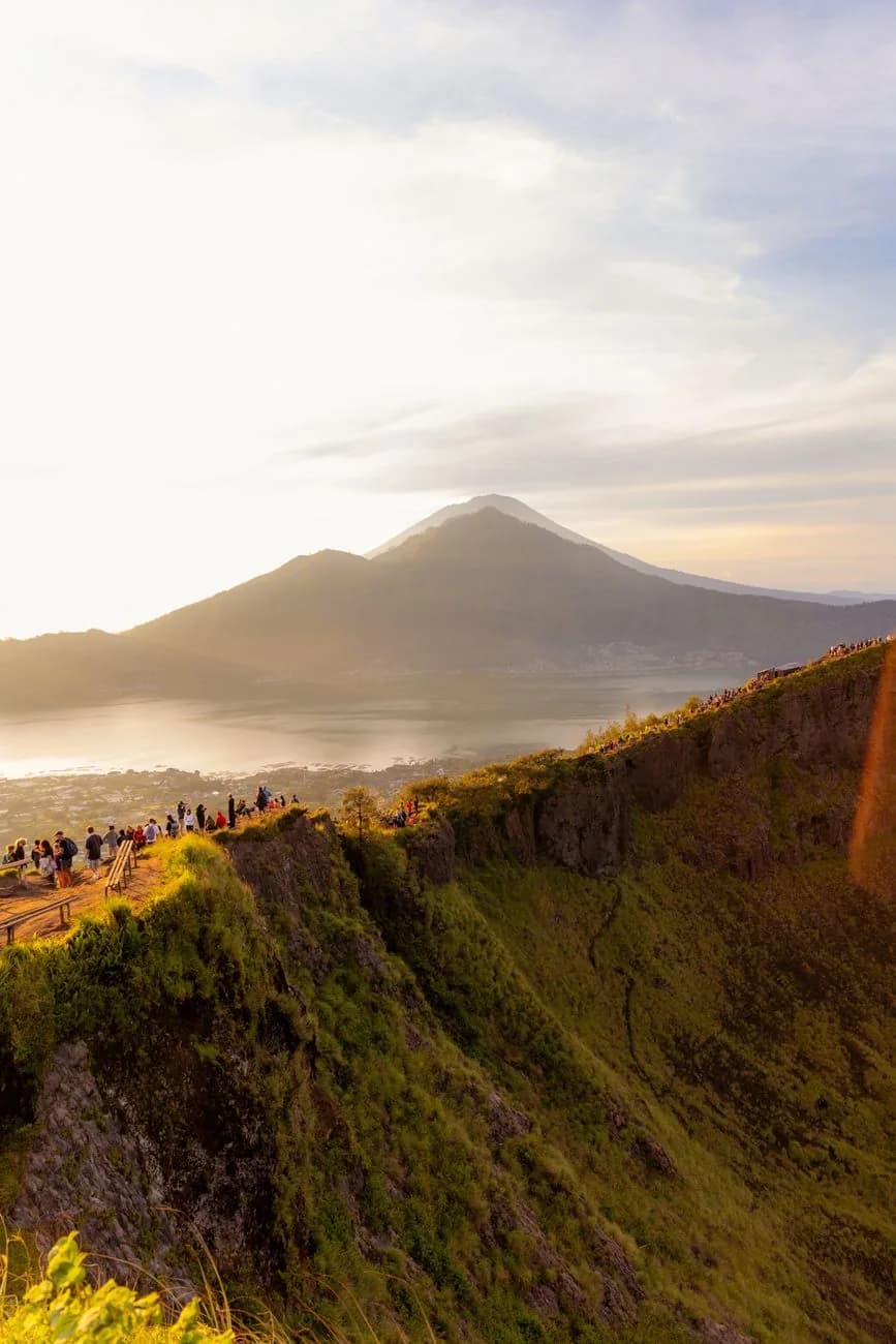 File de randonneurs sur la crête du mont Batur au lever du soleil, avec le lac Batur et le mont Abang en contrebas, Bali