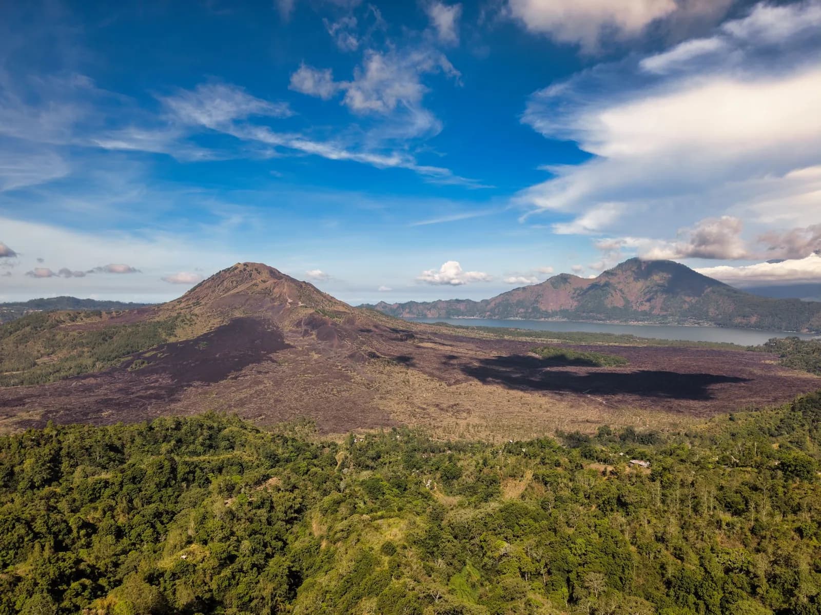 Vue aérienne du cône du mont Batur, de sa coulée de lave sombre et du lac Batur en contrebas, Bali